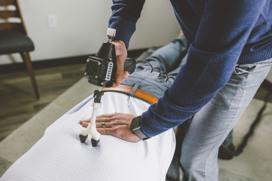 Chiropractor using ArthroStim adjusting tool on patient spine in modern clinic, professional environment