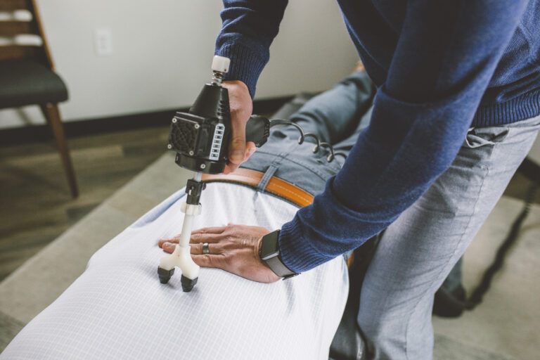 Chiropractor using ArthroStim adjusting tool on patient spine in modern clinic, professional environment